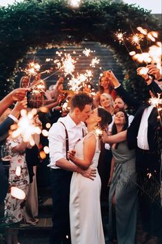 a bride and groom kiss as they are surrounded by their wedding guests with sparklers in the air