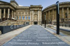 an empty walkway in front of a building with many words written on the sidewalk and steps leading up to it