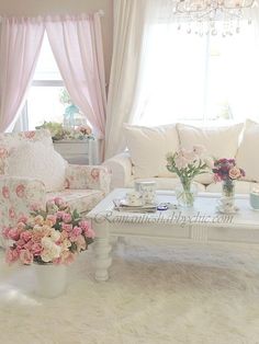 a living room with white furniture and pink flowers in vases on the coffee table