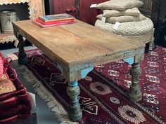 a wooden table sitting on top of a red rug next to a pile of pillows