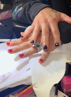 a woman's hands with red and black nail polishes on her nails, sitting at a desk