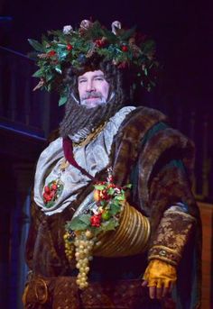 a man with a beard wearing a crown and holding grapes in his hand while standing on stage