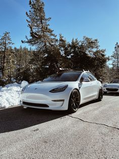 two white tesla cars parked in the snow