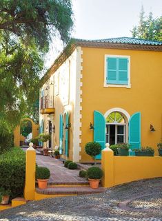 a yellow house with green shutters and blue windows on the outside, surrounded by greenery