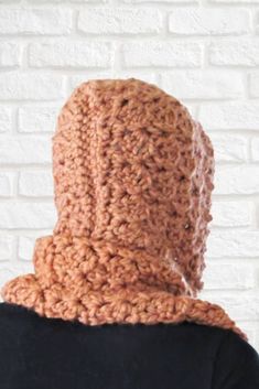 a person wearing a brown crochet cowl on top of their head in front of a white brick wall