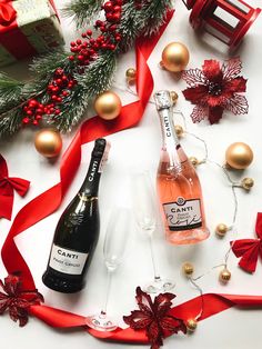 two bottles of champagne next to red ribbon and christmas decorations on a white surface with gold ornaments