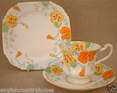 an orange flowered tea cup and saucer on a white plate with gold trim