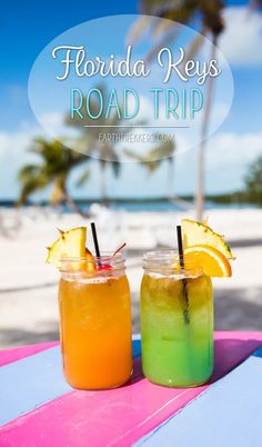 two drinks sitting on top of a table next to each other in front of the ocean