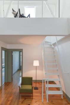 a living room with stairs leading up to the top floor and a green chair in front of it