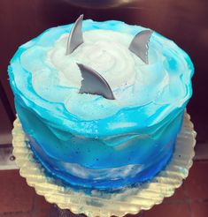 there is a blue cake with white frosting and two sharks on top, sitting on a plate