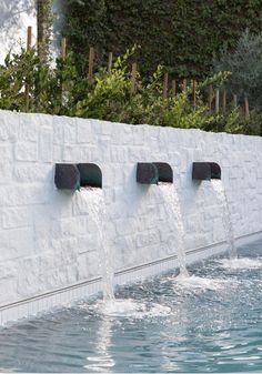 water gushing out from the side of a white wall into a pool with green plants growing on it