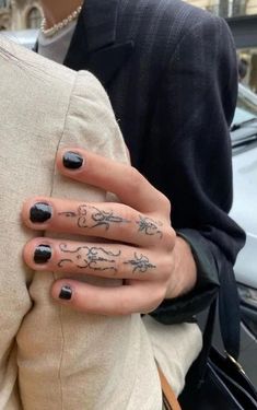 a woman's hand with black and white tattoos on her left thumb, holding onto the back of her jacket