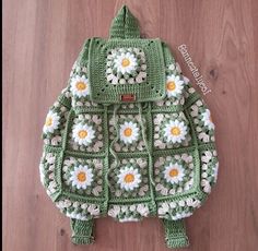 a crocheted green backpack with white flowers on the front and yellow petals on the back