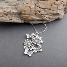 sterling silver dahlia flowers with butterflies necklace, 7/8" - A sterling silver charm, measuring 5/8" (15 mm) across and 7/8" (23 mm) down.   - Necklace is 1.5 mm cable chain, with lobster clasp and locking jump rings, all solid sterling silver.  - Charm has blackening (oxidizing) to bring out the details. - Flowers are realistic looking. Back is smooth and has a tiny 925 mark. - Packaged in a modern circular tin, ready for gift giving, and comes with a silver polish pad and care instructions Butterflies Necklace, Flowers With Butterflies, Dahlia Flowers, Silver Polish, Top Rings, Dahlia Flower, Natural Gifts, Butterfly Necklace, Nature Jewelry