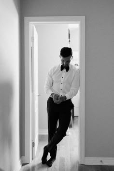 a man in a bow tie is looking at his cell phone while standing in the hallway