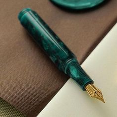 a pen sitting on top of a notebook next to a green and white plate with a brown cover