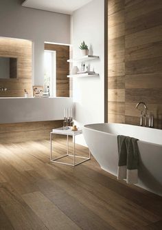 a large white bath tub sitting on top of a wooden floor next to a sink