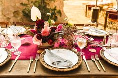 a table set with plates, silverware and pink napkins for an outdoor dinner