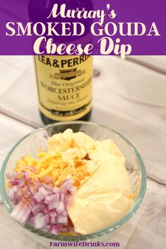 a glass bowl filled with cheese and onions next to a bottle of wine on a wooden table