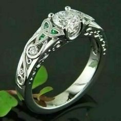 a white gold engagement ring with green accents