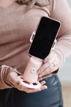 a woman holding an electronic device in her hands and showing it to the camera with both hands