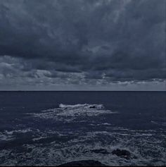 dark clouds over the ocean with waves coming in from the shore and one boat on the water