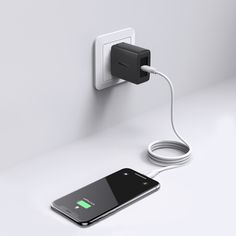 an iphone charging with a charger attached to the wall next to it on a white surface