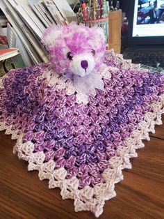 a purple and white crocheted teddy bear sitting on top of a wooden table