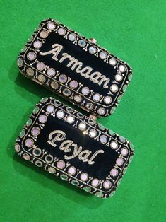 two black and white brooches with the word aman on them sitting on a green surface