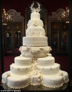 a large white wedding cake sitting on top of a glass table in front of chandeliers