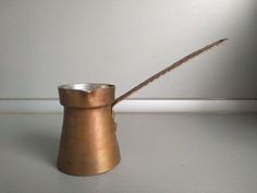 a small metal cup with a wooden stick sticking out of it's side next to a wall