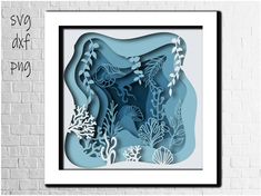 an image of paper cut art with seaweed and corals in blue tones on a white brick wall