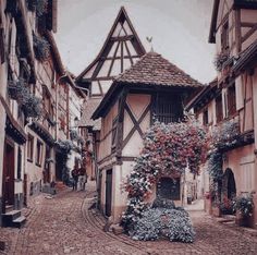 an old european street with flowers growing on the buildings and cobblestone road leading up to it