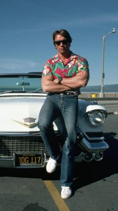 a man sitting on the hood of an old car with his arms crossed in front of him