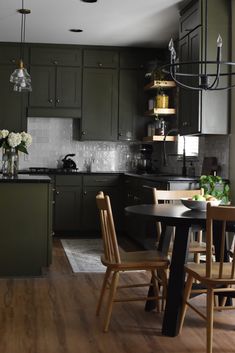 a kitchen filled with green cabinets and wooden chairs next to a dining room table in front of a stove top oven