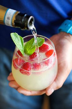 a person holding a wine glass filled with ice and raspberry spritz