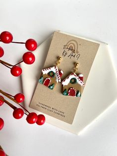 a pair of earrings sitting on top of a card next to some red berry branches