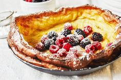 a pastry dish with berries and powdered sugar on the top, next to a cup of coffee