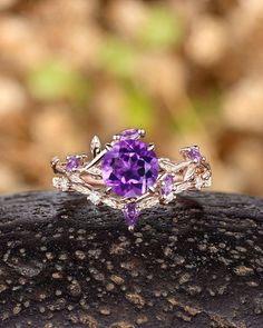 an amethorate ring is shown on top of a piece of wood with leaves and stones around it