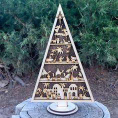 a wooden christmas tree on top of a stump in front of some bushes and trees