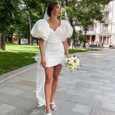 a woman in a short white dress is walking down the street with her wedding bouquet