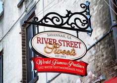 the sign for river street sweets is hanging from the side of an old brick building