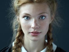 a young woman with blue eyes wearing a black shirt and braided hair is looking at the camera