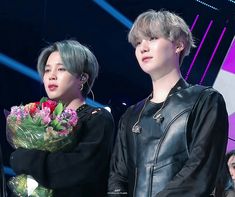 two people standing next to each other with flowers in their hands and one person wearing a black leather jacket