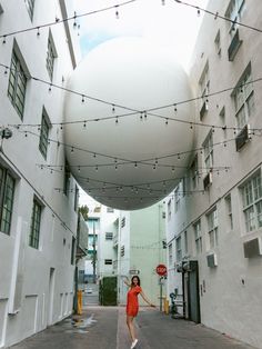 a woman in an orange dress is walking down the street with string lights strung over her