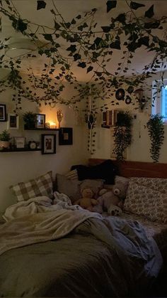 an unmade bed in a room with plants hanging from the ceiling and pictures on the wall