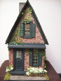 a doll house with green shutters and flowers on the front door is sitting on a table