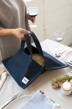 a person holding a blue bag over a table with plates and wine glasses on it