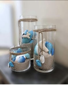 three glass vases filled with sand and seashells