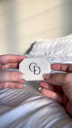 two hands are holding a white object with the letter p on it in front of a bed